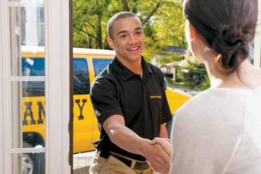 Smiling Stanley Steemer technician warmly greets customer at the front door on a sunny spring day