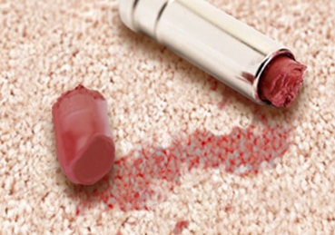 Broken lipstick tube laying on carpet with lipstick stains. 