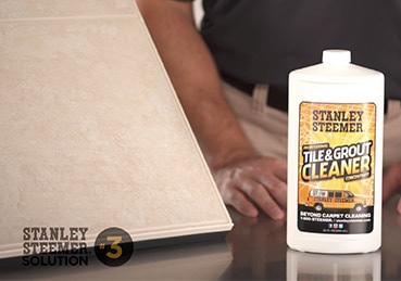 Bottle of Stanley Steemer Tile and Grout Cleaner sitting next to a tile slab. 