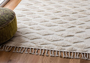 Cream-colored area rug with a diamond pattern and fringe laying on a hardwood floor